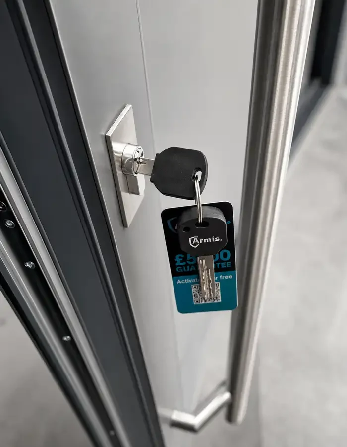 Close up of a high-security lock on an aluminium front door showing the Armis security key and the five thousand pound guarantee tag.